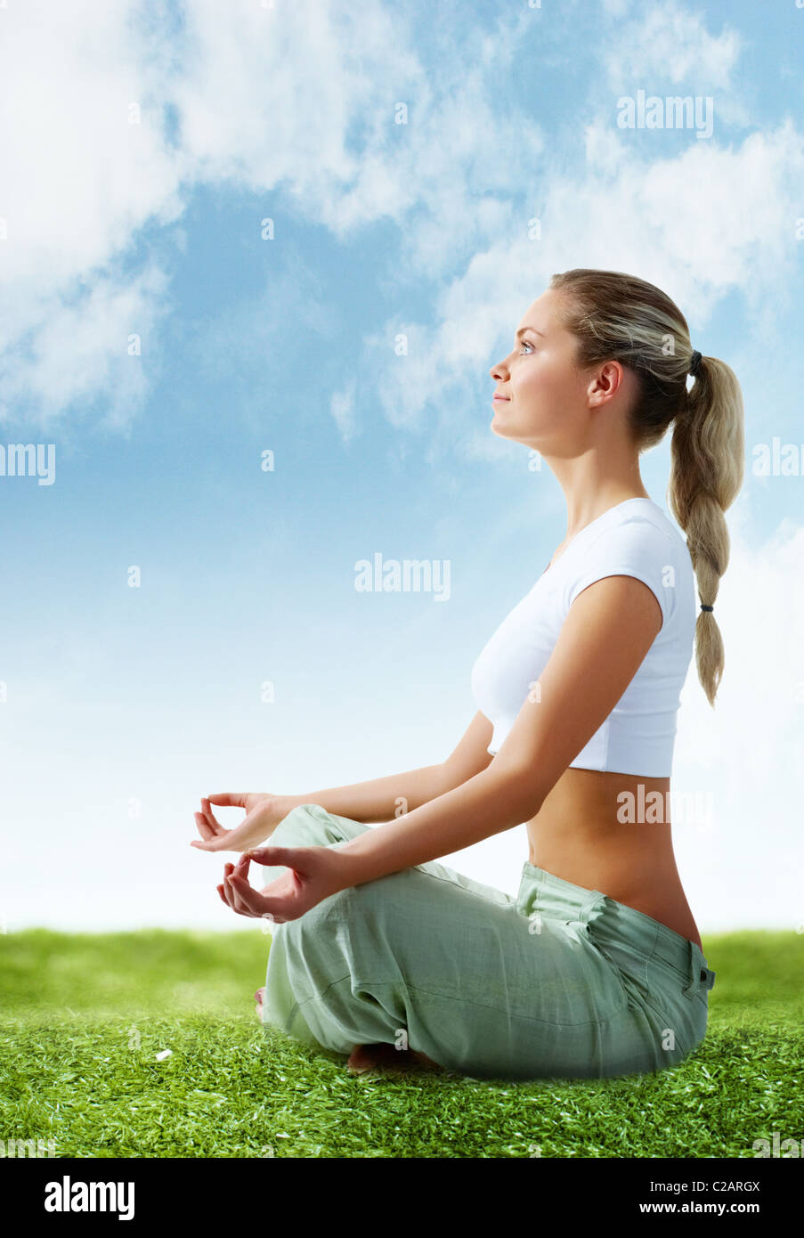 Portrait of young woman meditating in pose of lotus on green grass ...