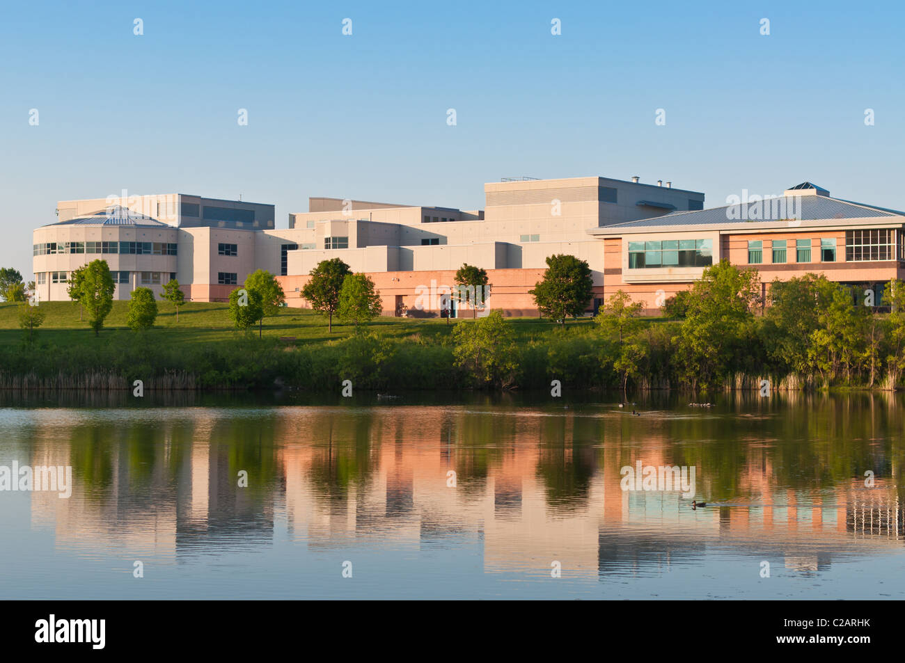 A community center building surrounded by a park is shown reflected in the water of a large pond. Stock Photo
