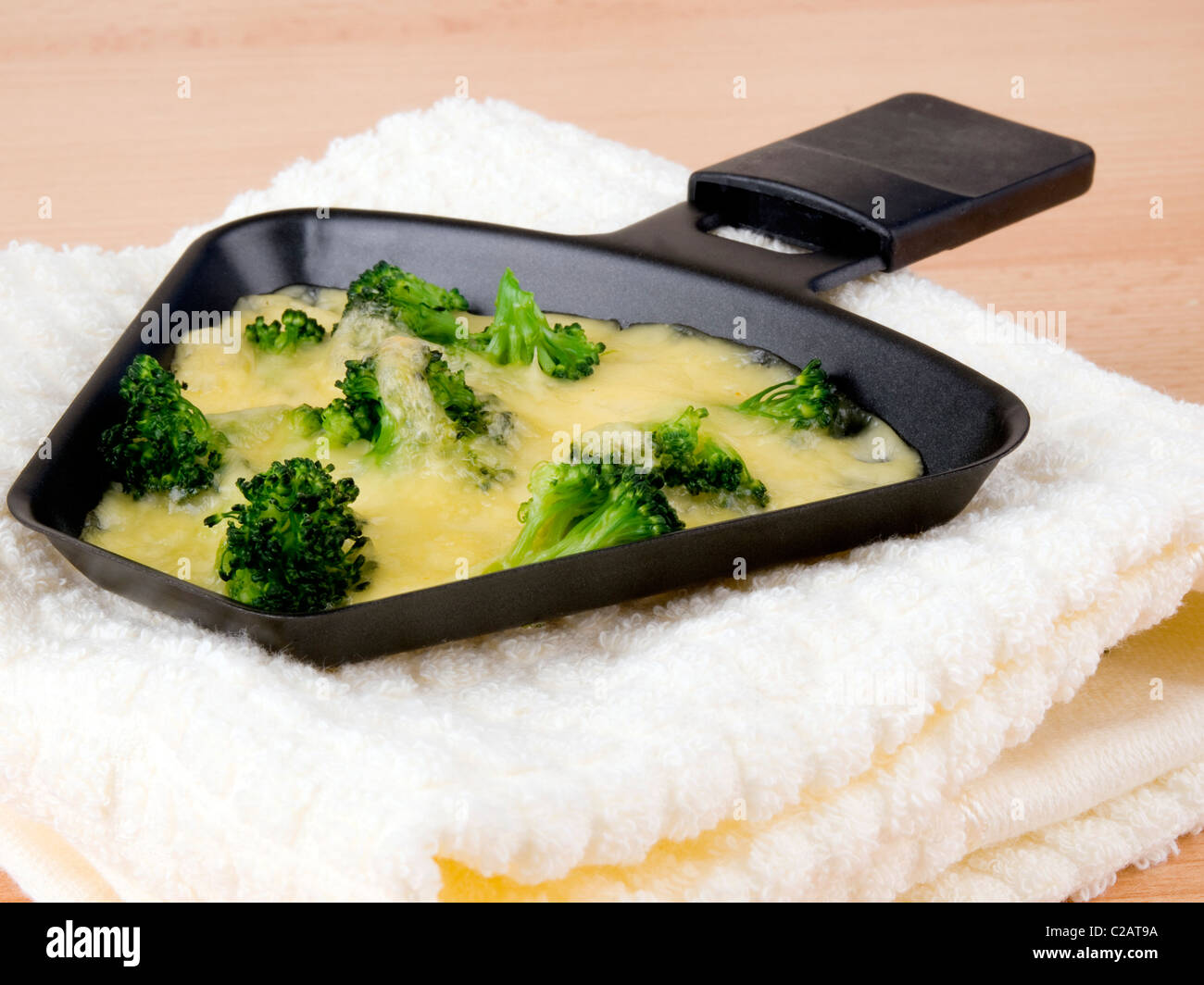 Raclette pan with cheese and broccoli laing on soft napkin Stock Photo ...