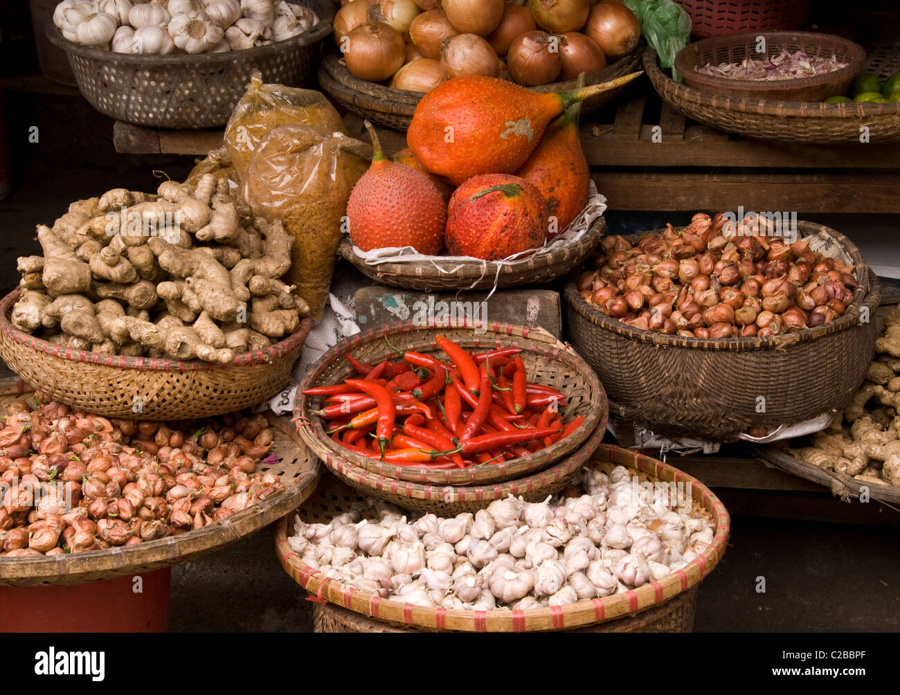 Baskets of gac fruit, chilli, onions, shallots, ginger and garlic at a market in the Hanoi Old Quarter, Viet Nam Stock Photo