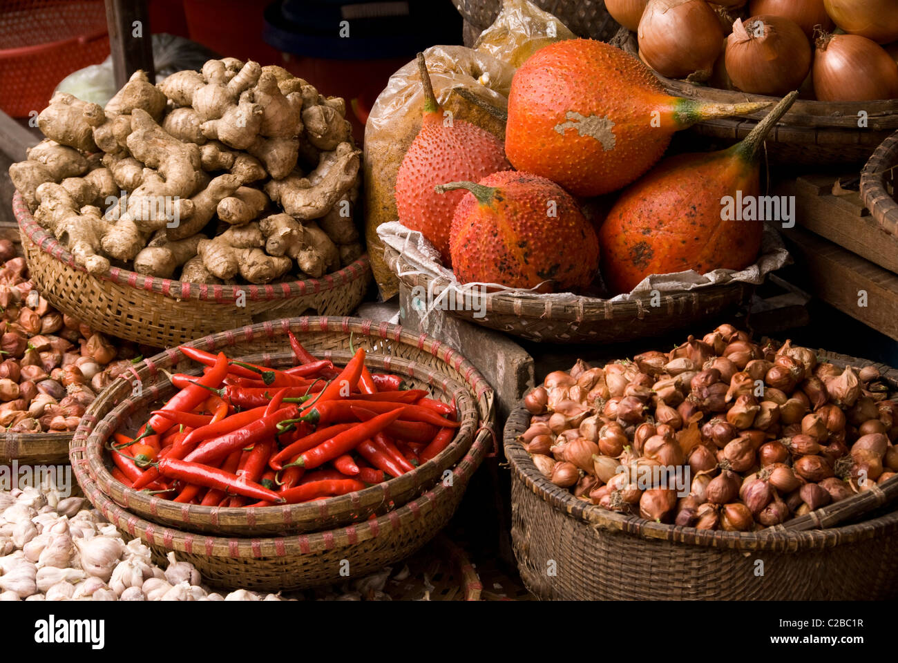 Baskets of gac fruit, chilli, onions, shallots, ginger and garlic at a market in the Hanoi Old Quarter, Viet Nam Stock Photo