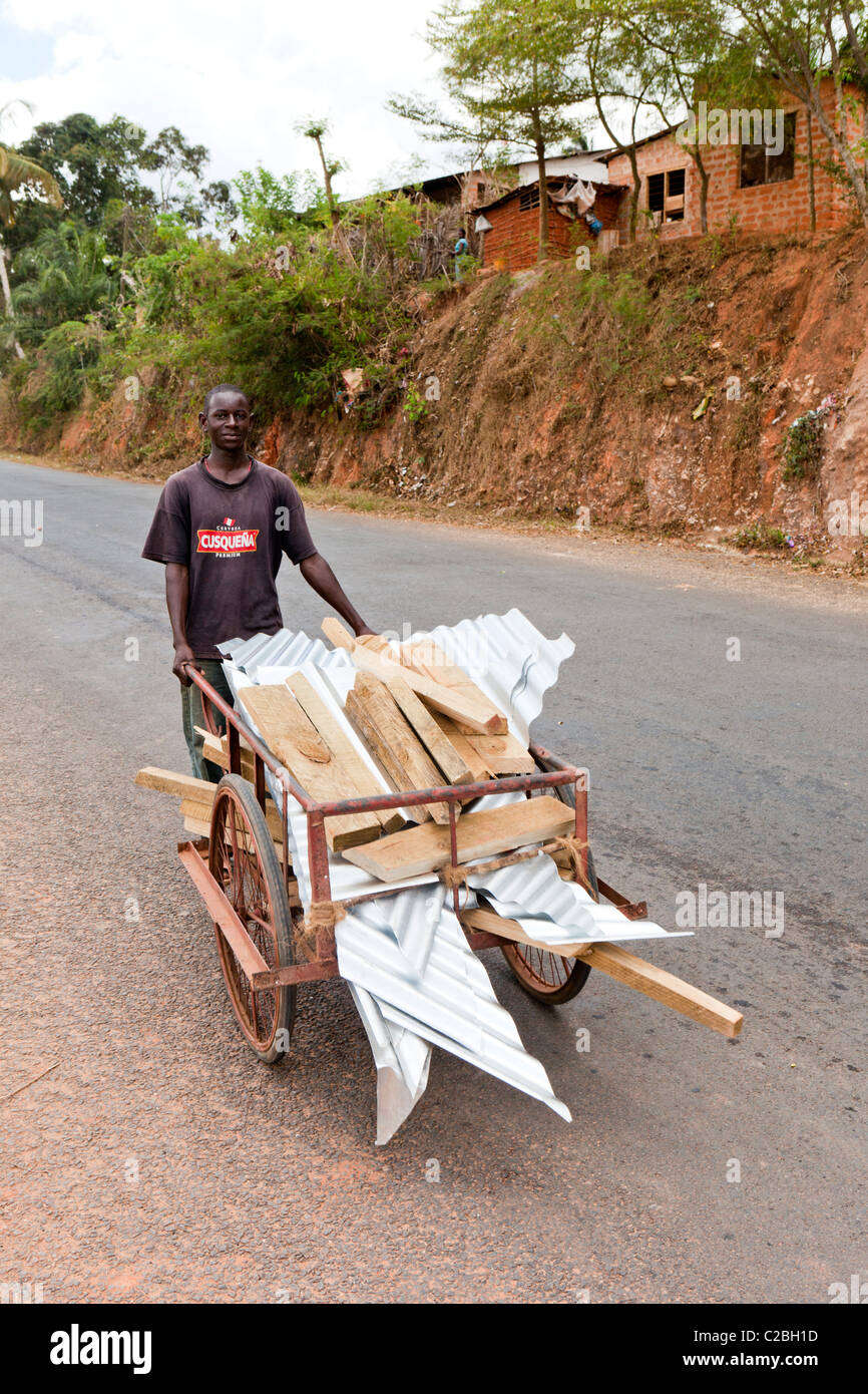 A man walking down a hill with a push cart of corrugated tin roofing. Kisarawe Village Dar es Salaam Tanzania. Stock Photo