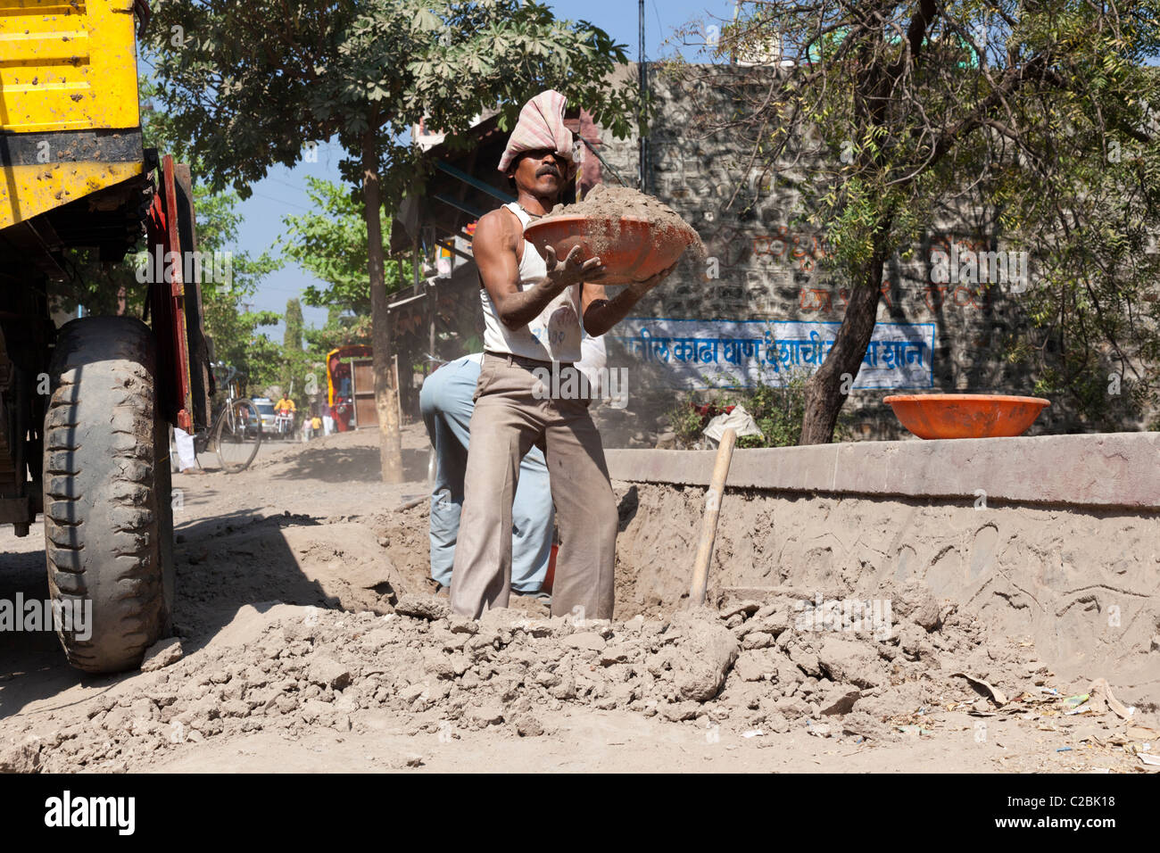 Male construction worker lifting a heavy load of sand at a road works site, Valsang, Maharashtra, India Stock Photo