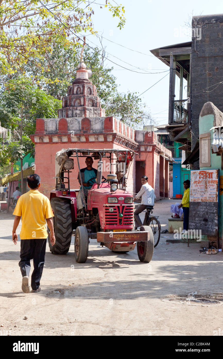 Red tractor passing a Hindu temple in a village street, Valsang, Maharashtra, India Stock Photo