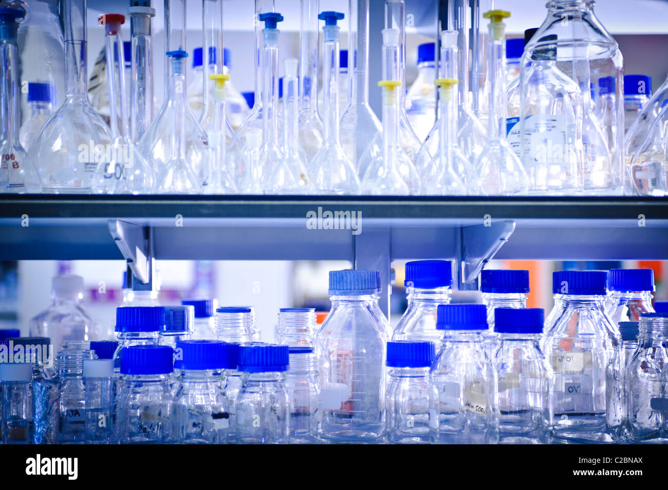 Glass bottles and jars beakers and test tubes with bright blue tops on shelf in science laboratory Stock Photo