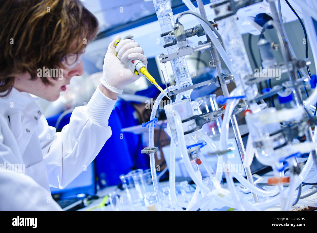 Young male scientist wearing goggles and white lab coat pipetting into