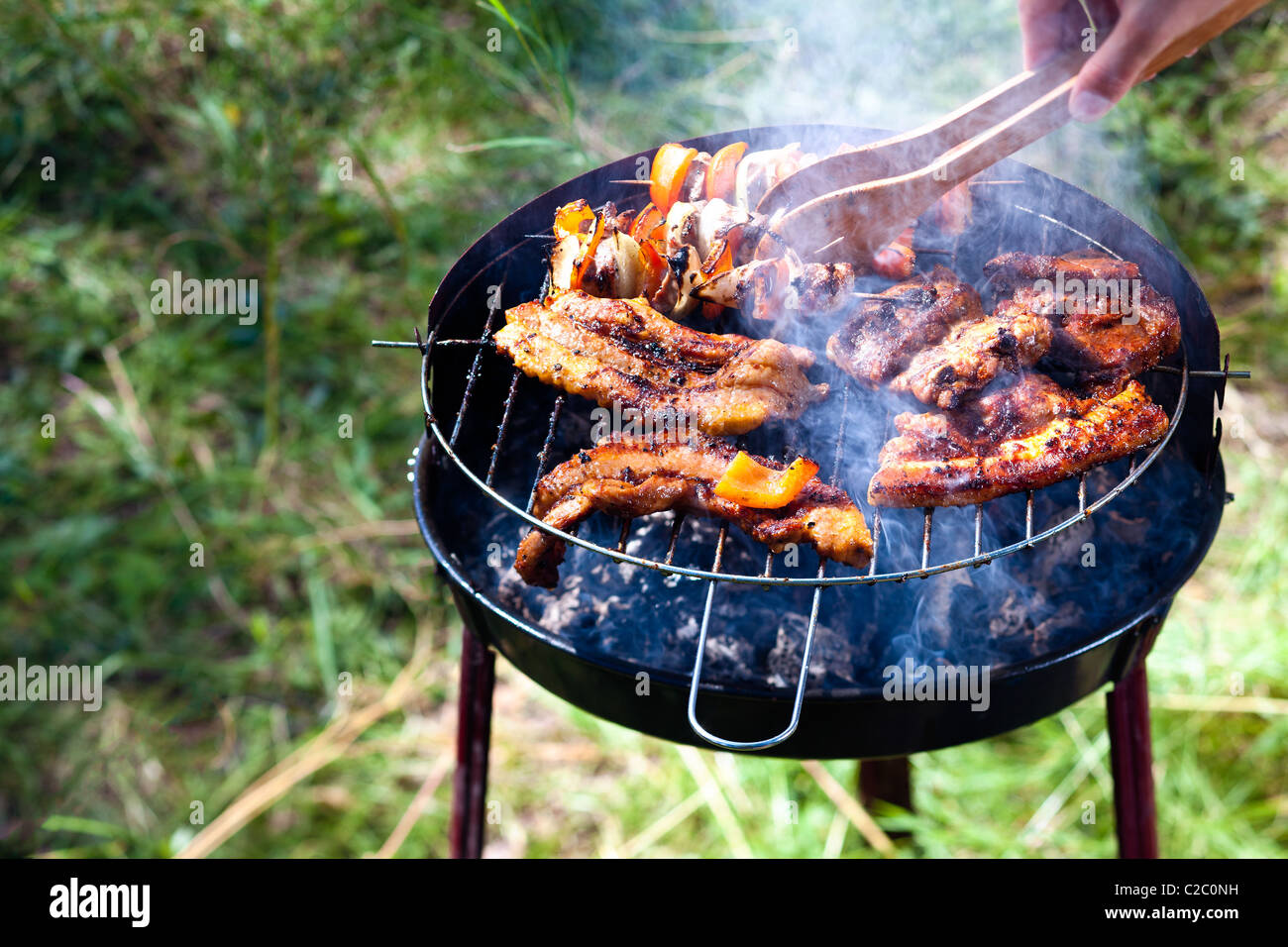 hand turning barbeque on the grill with tongs with nice bit of smoke  visible Stock Photo - Alamy