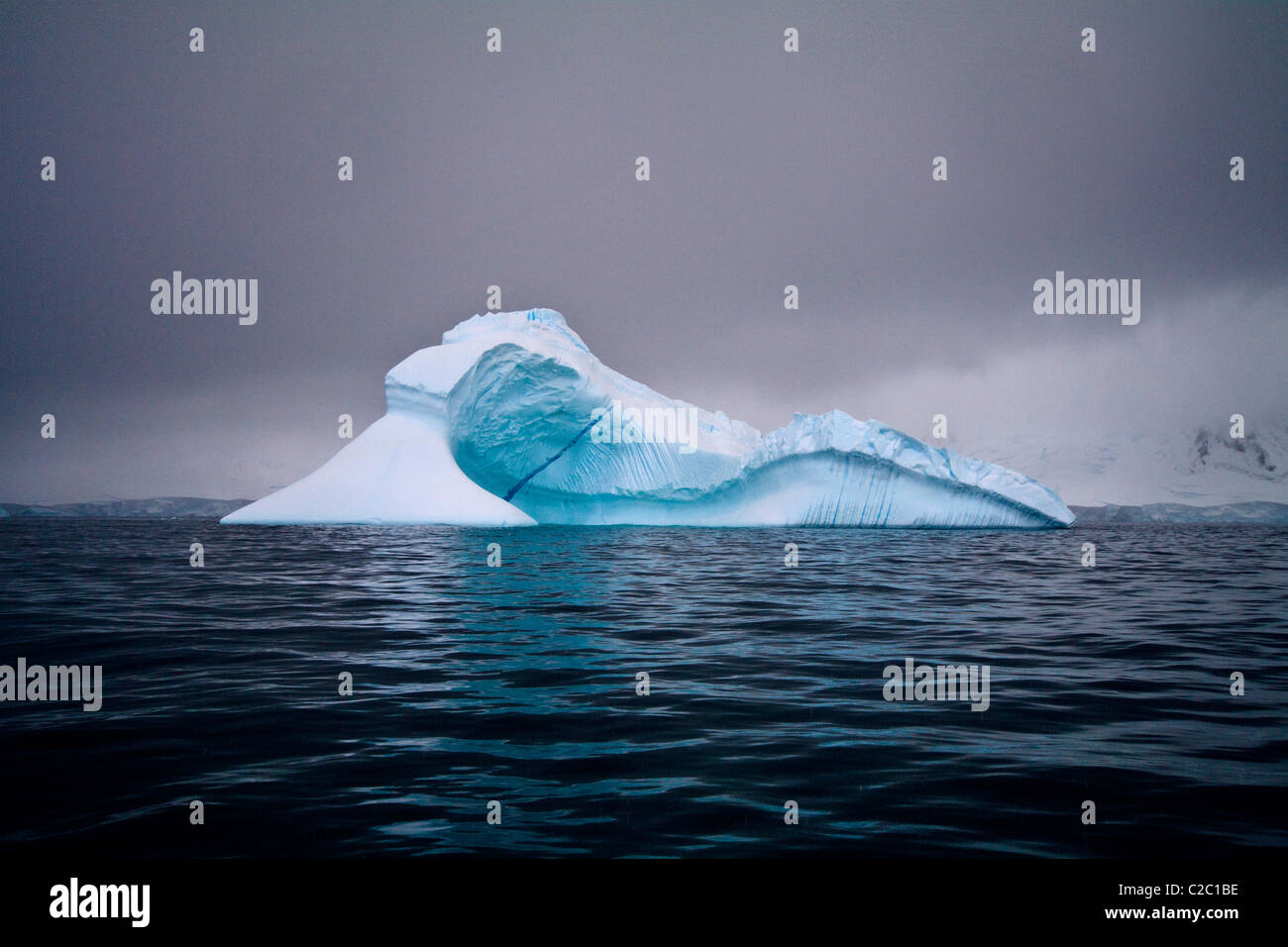 An iridescent iceberg floating in a dark sea beneath stormy skies. Stock Photo