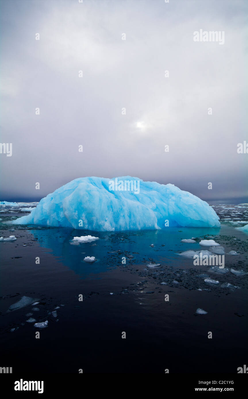 The sun casts ghostly reflected light over an iridescent blue iceberg. Stock Photo