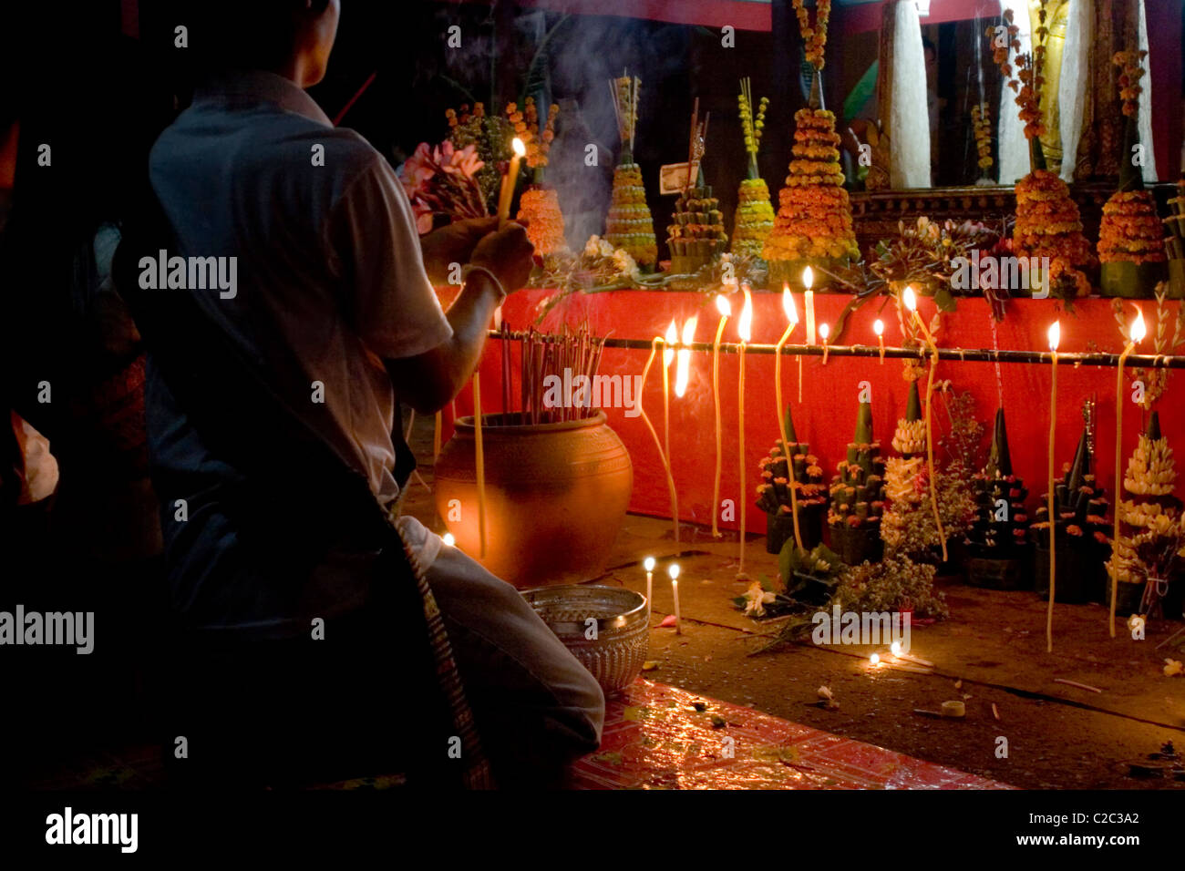 People are gathered with candles to pay tribute to the Pra Bang Buddha at a Buddhist temple in communist Laos. Stock Photo