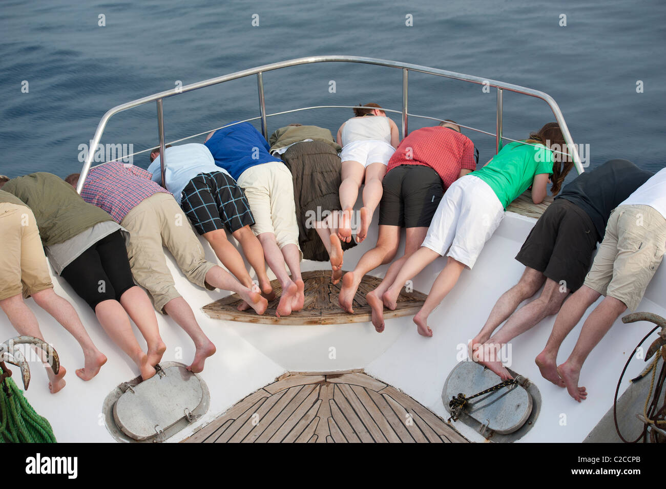 Group of people hanging over the boat bow looking for dolphins Stock Photo