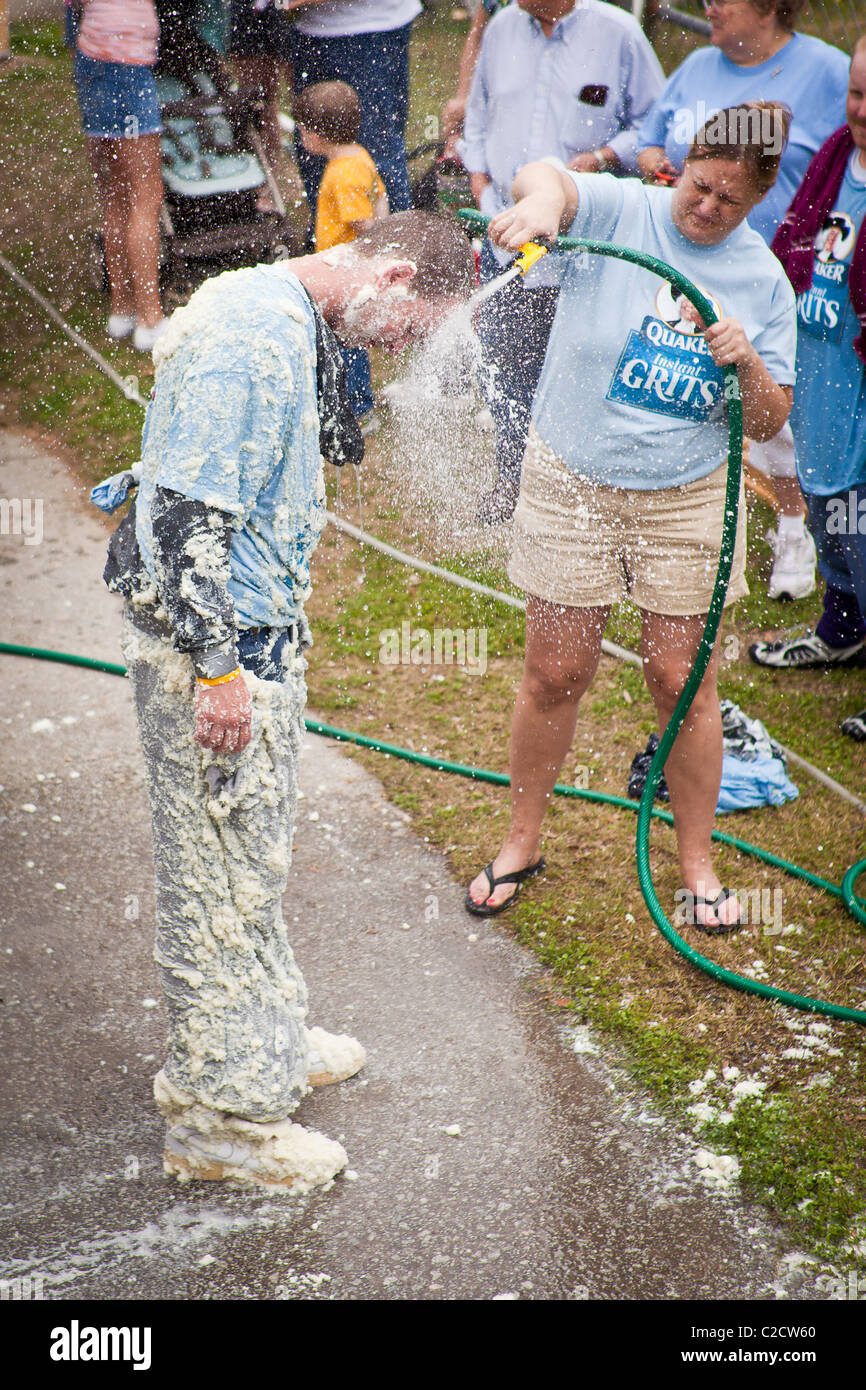 A participant in the Grits Roll is hosed down after wallowing in a pool of grits during the annual World Grits Festival in St Ge Stock Photo