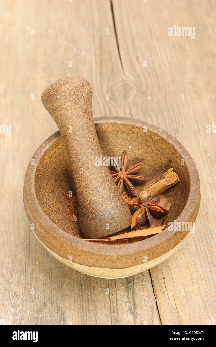 A stoneware pestle and mortar with star anise and cinnamon spices on a background of old cracked wood Stock Photo