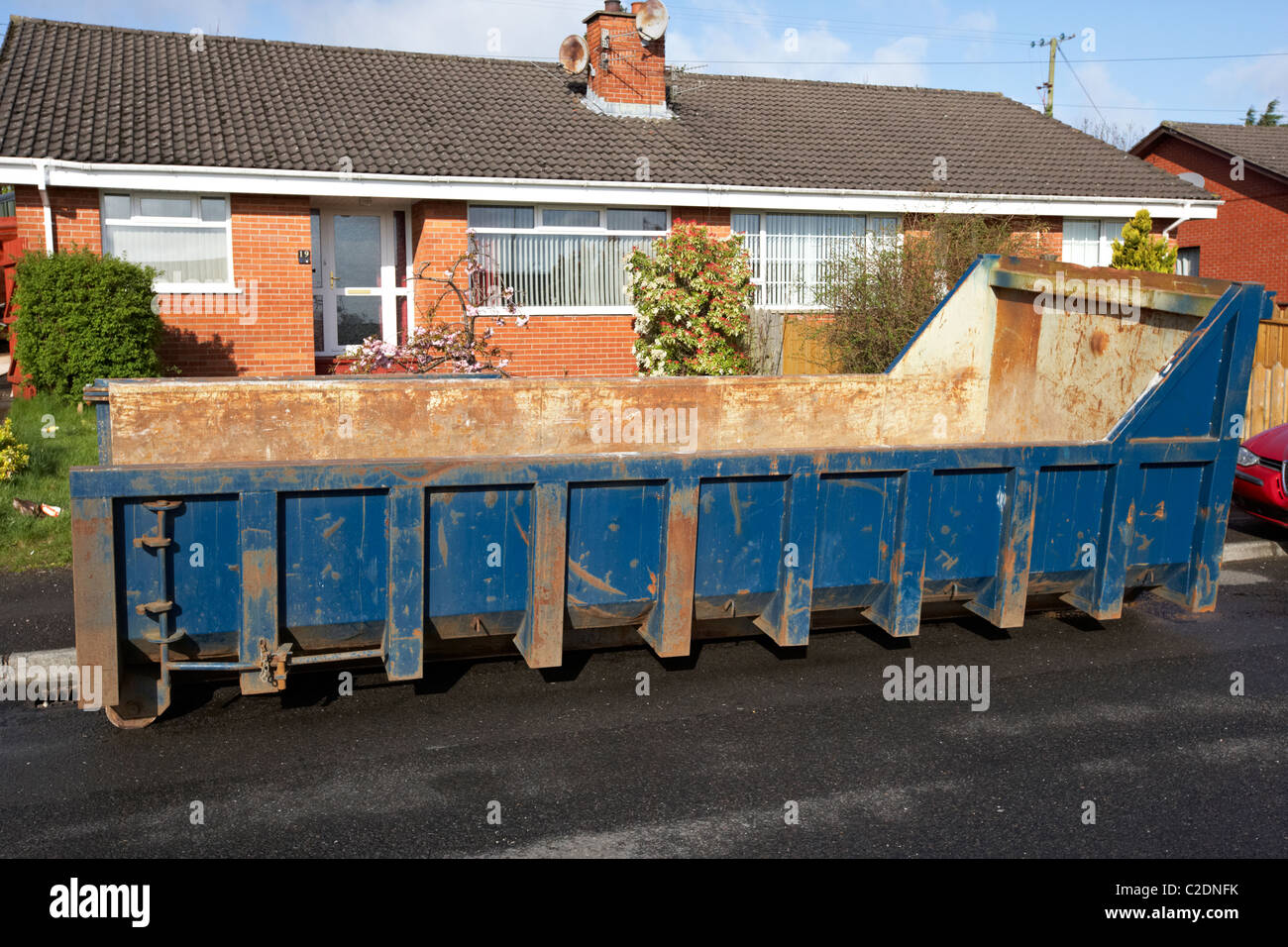 large roll on off building skip placed outside a row of houses in the uk Stock Photo