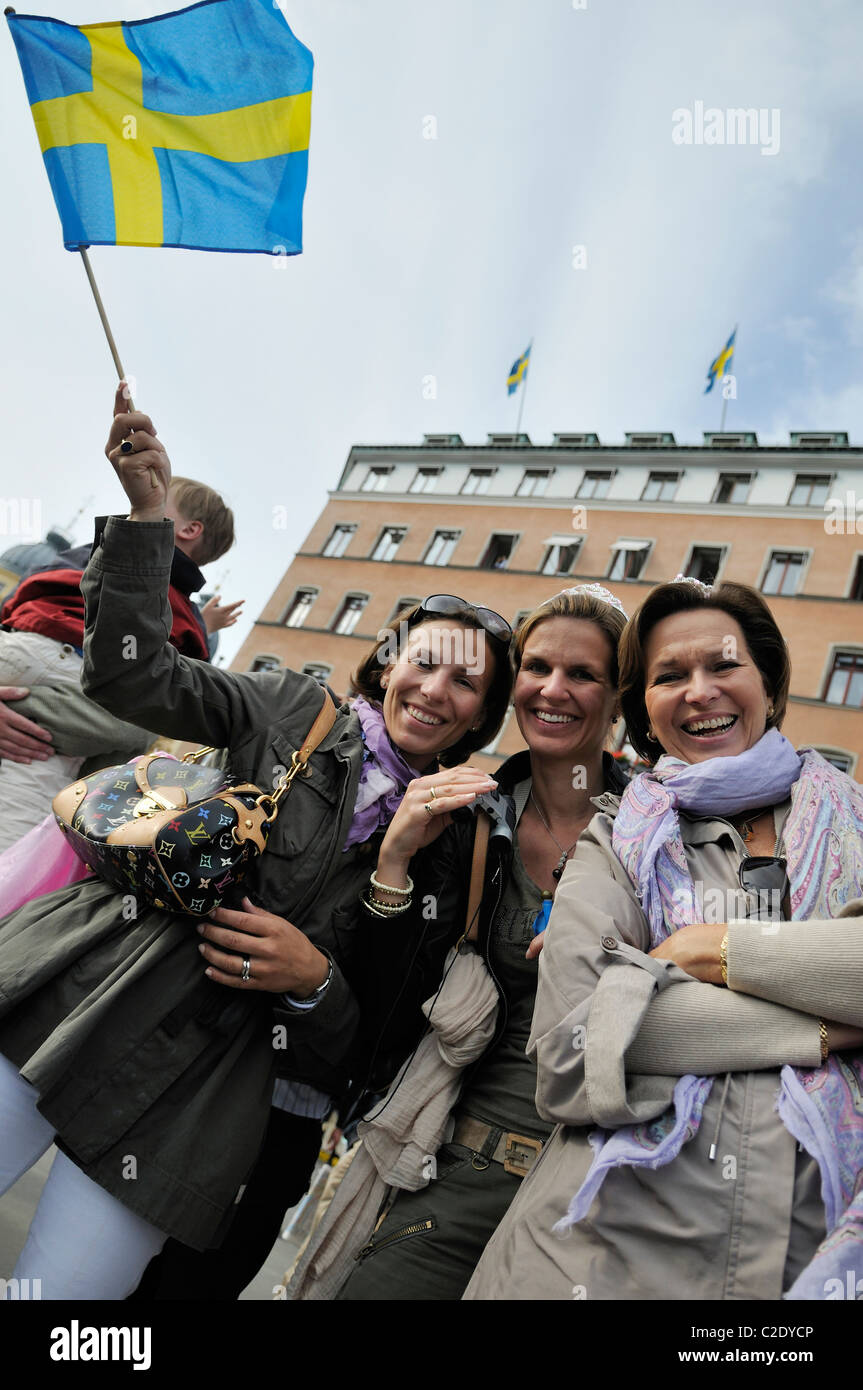 Three middle-aged women smiling and waving little Swedish flag during the Royal Wedding Festivities in Stockholm, Sweden Stock Photo