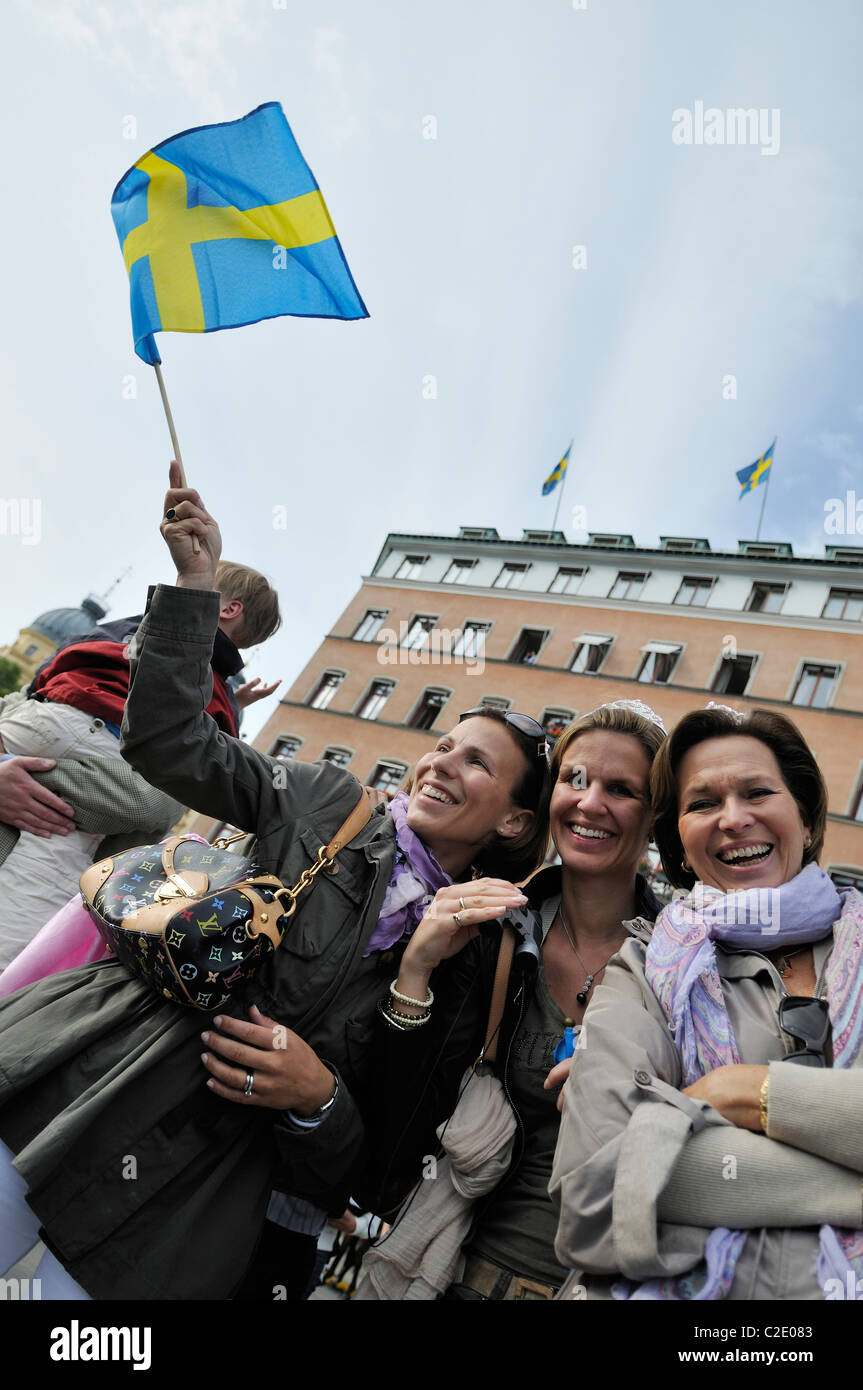 Three middle-aged women smiling and waving little Swedish flag during the Royal Wedding Festivities in Stockholm, Sweden Stock Photo