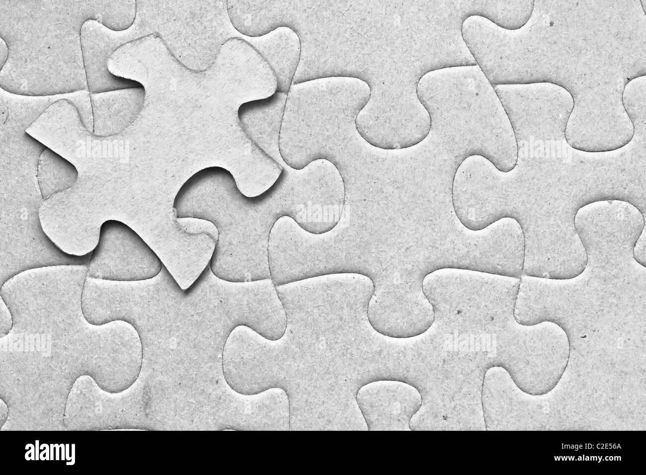 Complete grey cardboard jigsaw puzzle with one floating piece on top