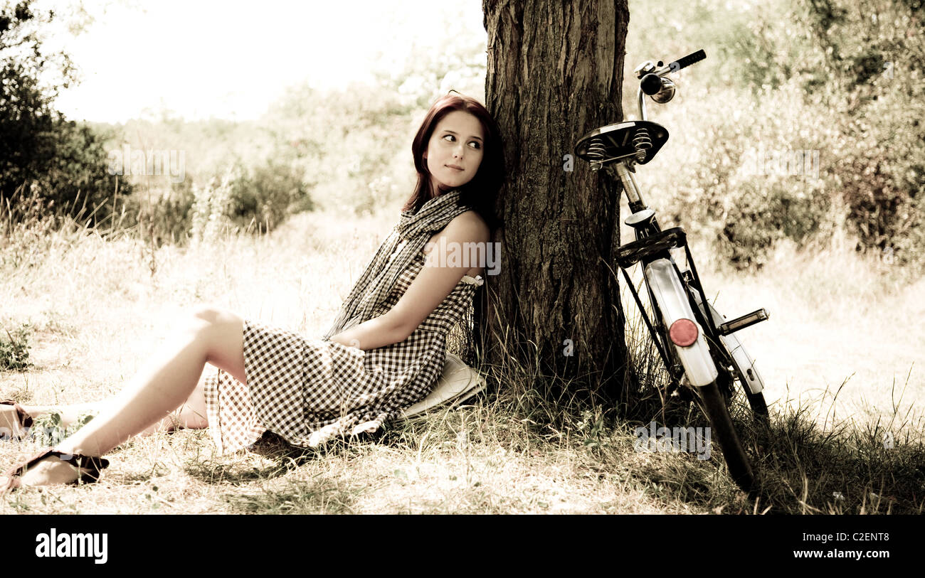 Beautiful girl sitting near bike and tree at rest in forest. Stock Photo