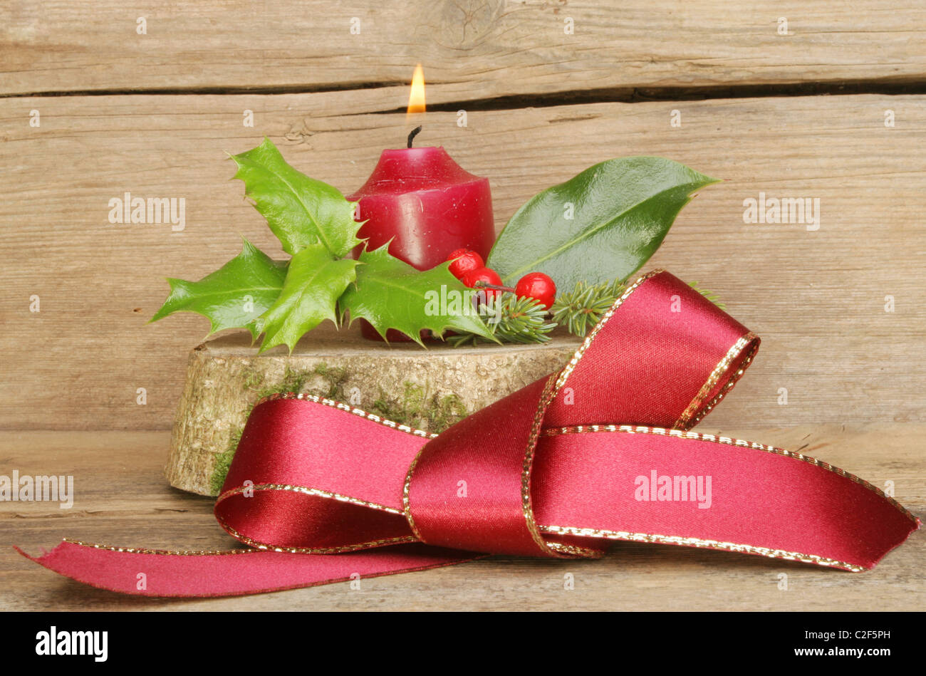 Red ribbon bow and Yule log with a burning candle on a background of old weathered wood Stock Photo