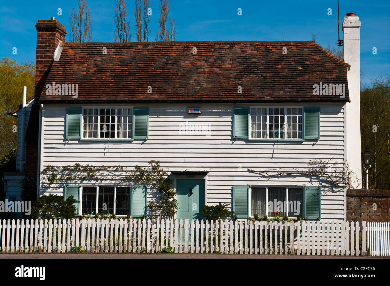 White Country Cottage With Blue Window Shutters and A Picket Fence Stock Photo