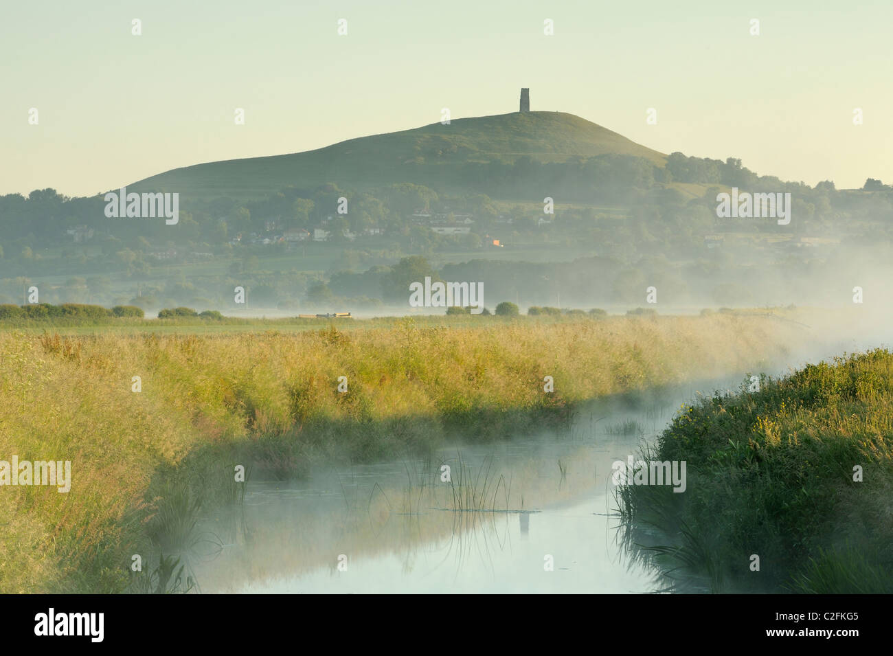 The River Brue with Glastonbury Tor in the distance during a misty sunrise on the Somerset Levels. Stock Photo
