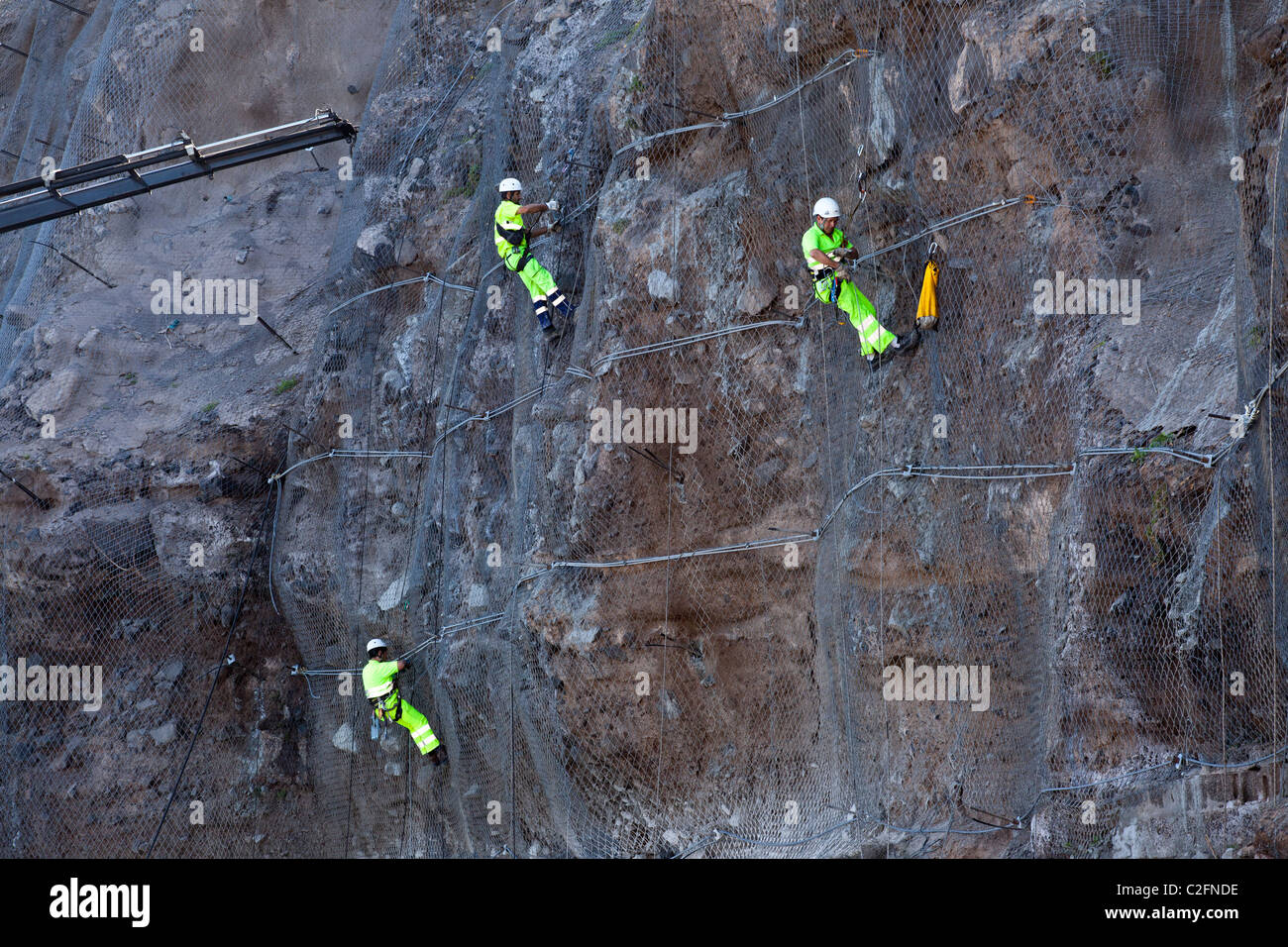 Workers in bright yellow clothing reinforce the cliff face at Los Gigantes, Tenerife Stock Photo