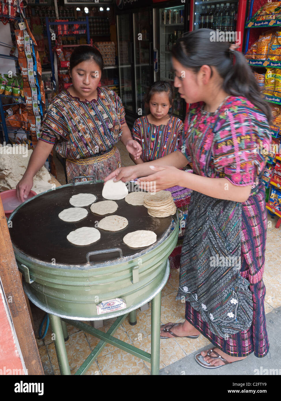 Two woman cook tortillas for sale on a grill just inside a small store