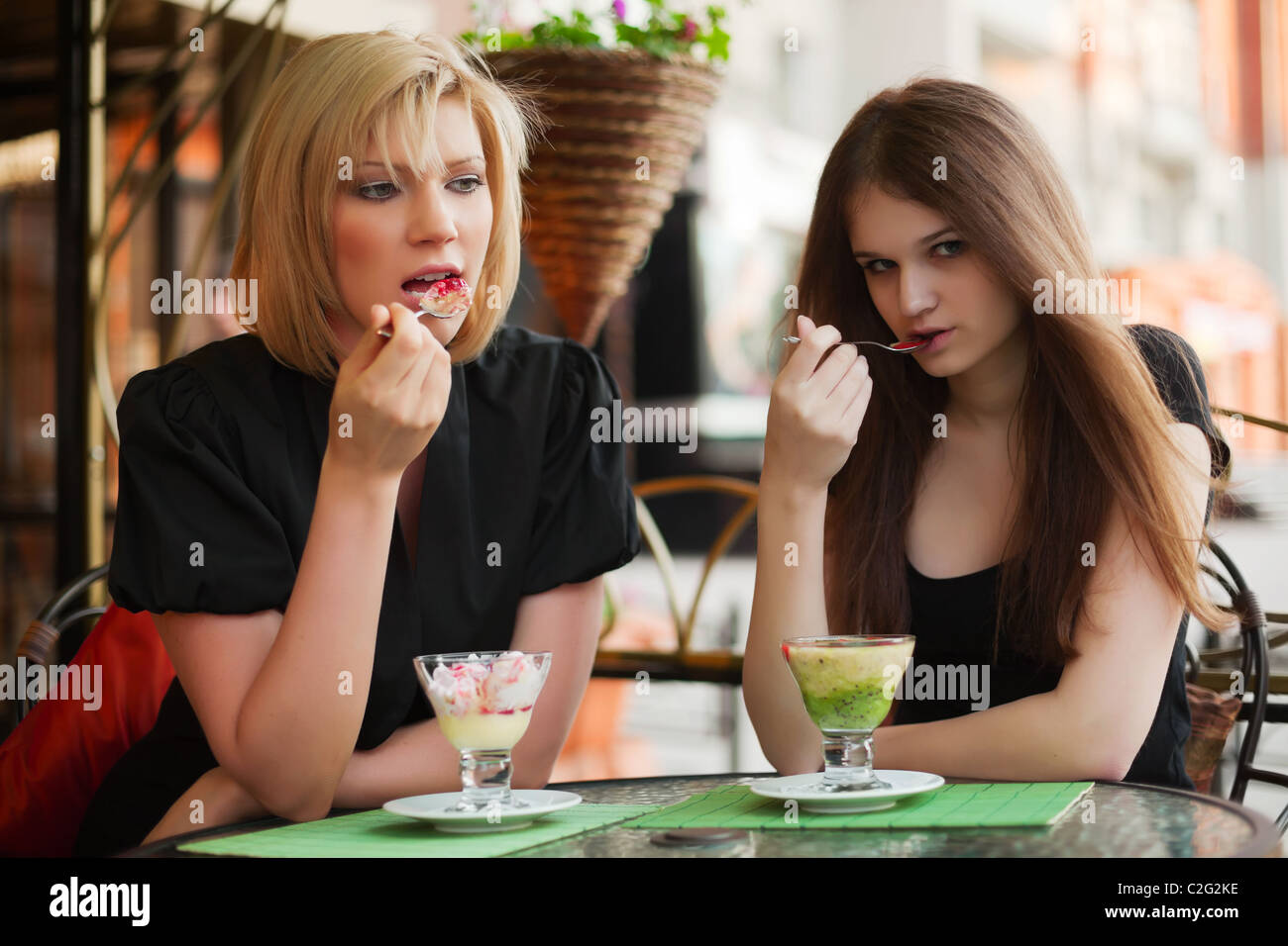 Two young women eating an ice cream at sidewalk cafe Stock Photo