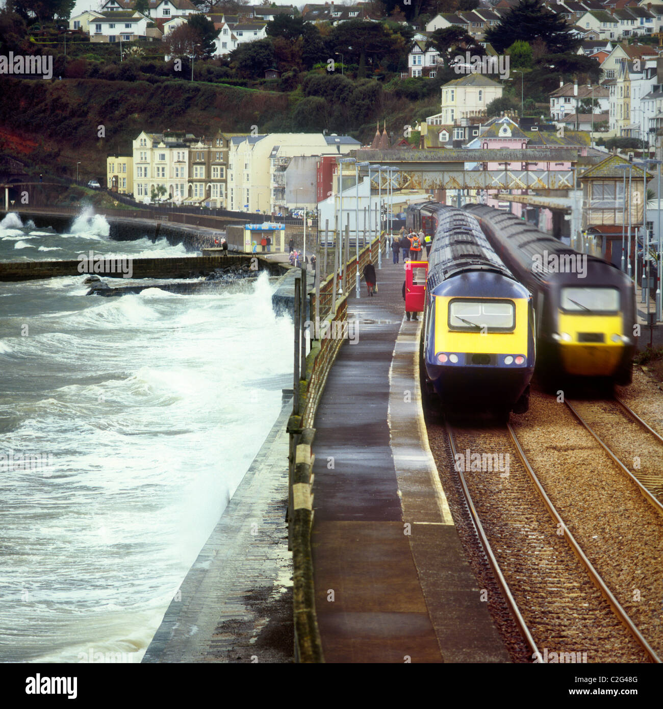 Plymouth-bound First Great Western high speed train calls at Dawlish station while Cross Country HST passes through at speed. Stock Photo