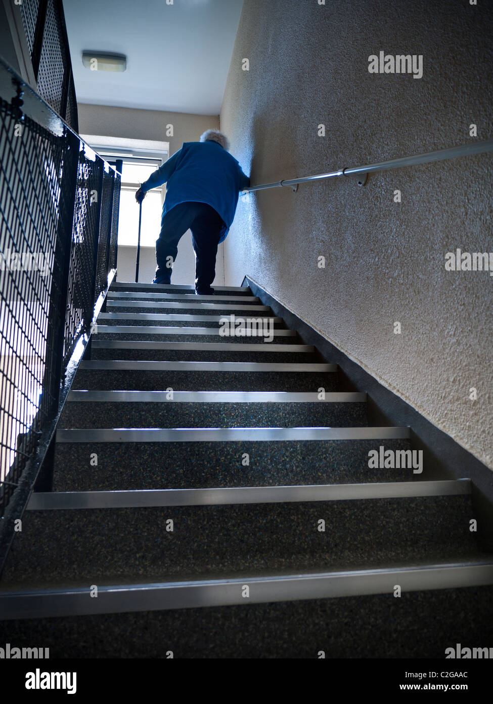 ELDERLY CLIMBING STAIRS IN FLAT HOME Independent elderly senior pensioner lady at 97 years climbing steep flight of stairs aided by her walking stick Stock Photo