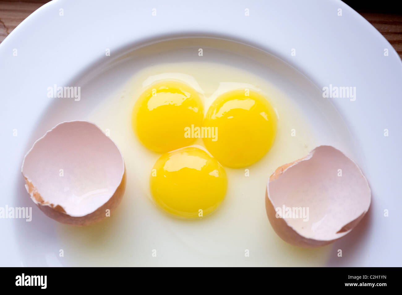 A rare triple yolk farm egg on a plate with its egg shell Stock Photo
