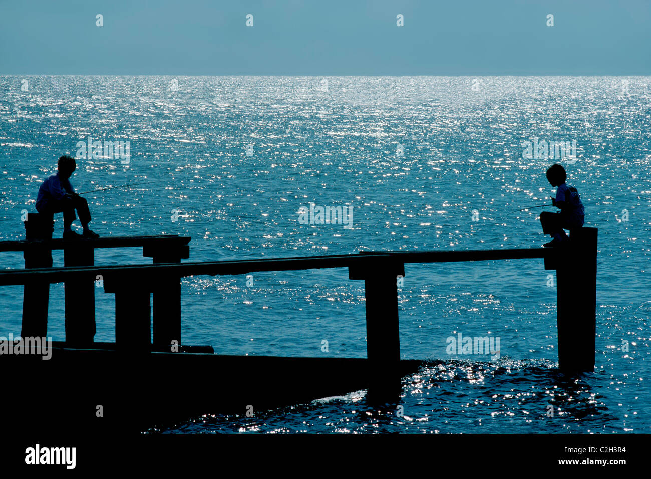 Two young boys are silhouetted by the glistening waters of the Gulf of Mexico as they fish from pilings at Cedar Key on the west coast of Florida, USA. Stock Photo