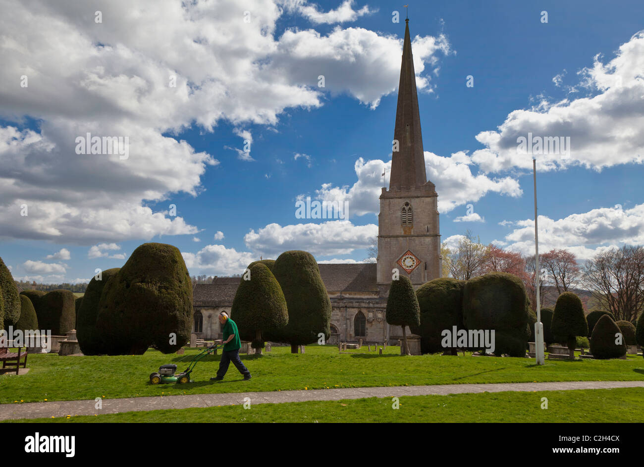 PAINSWICK CHURCH YARD WITH YEW TREES AND MAN CUTTING GRASS Stock Photo