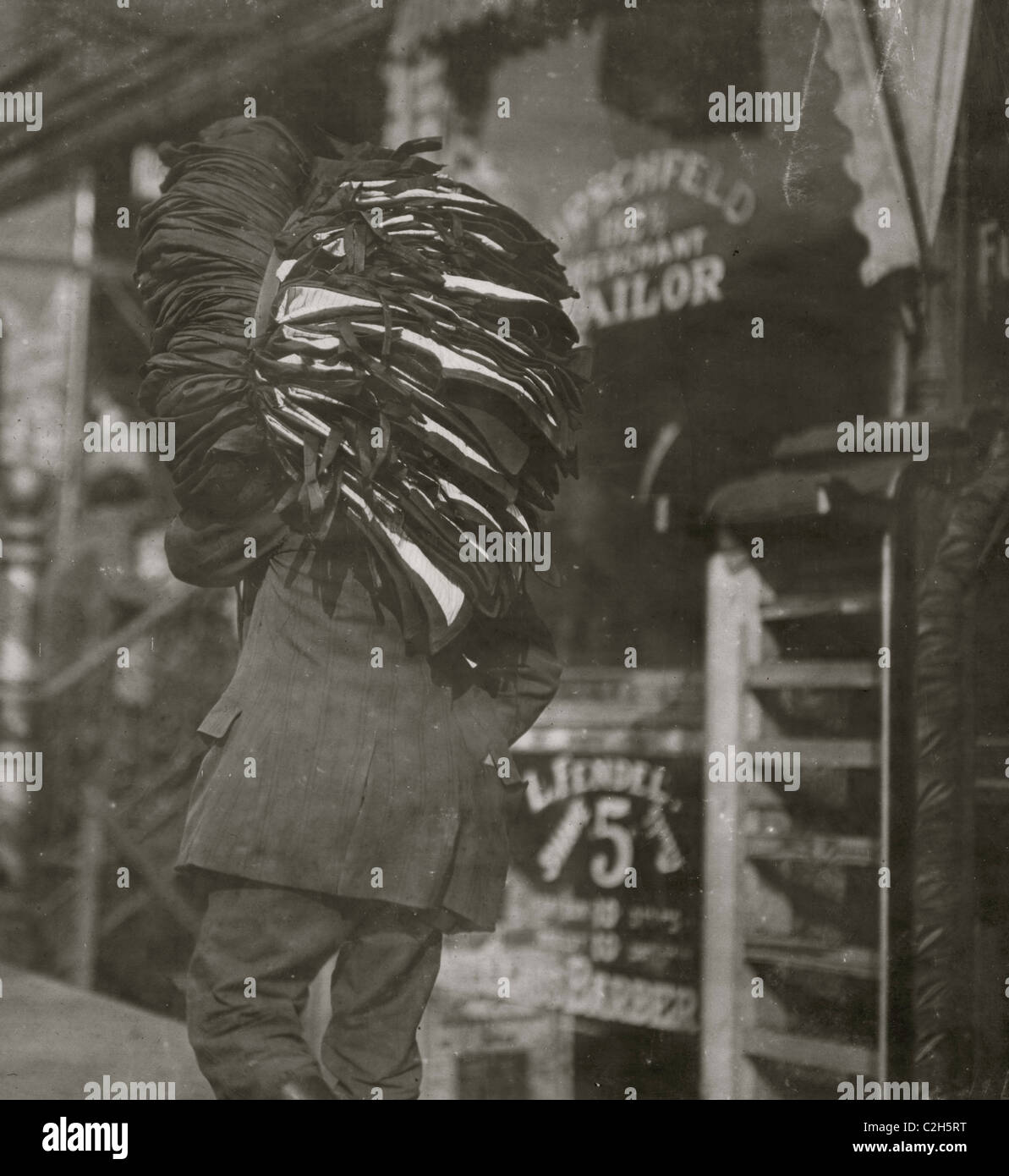 Man loaded down with heavy bundle of vests that he had been carrying for many blocks, stopping to rest, occasionally, when he would drop the bundle down onto whatever boxes or railings were available, even though they were dirty Stock Photo
