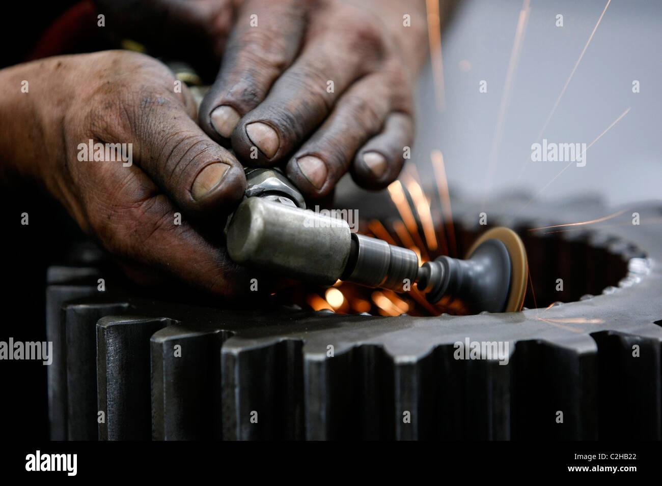 Machinist's dirty hands working with grinding tool with sparks flying. Stock Photo