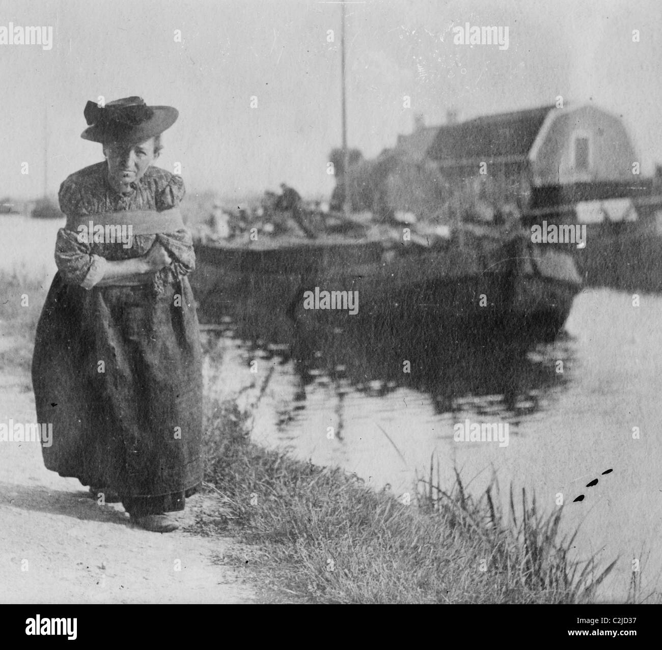 A Older Dutch woman has a bustle around her chest as she pulls a barge down a canal. Stock Photo