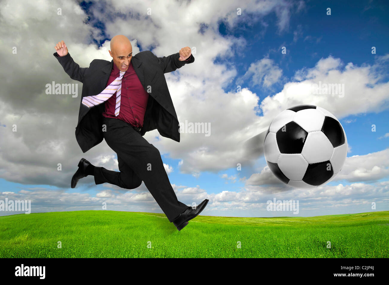 Businessman in a acrobatic pose kicking a soccer ball in a green field  Stock Photo - Alamy