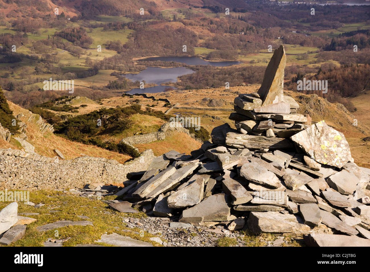 Stone cairn by path and dry stone wall on Lingmoor Fell with Elterwater below, Langdale, Cumbria, England, UK Stock Photo