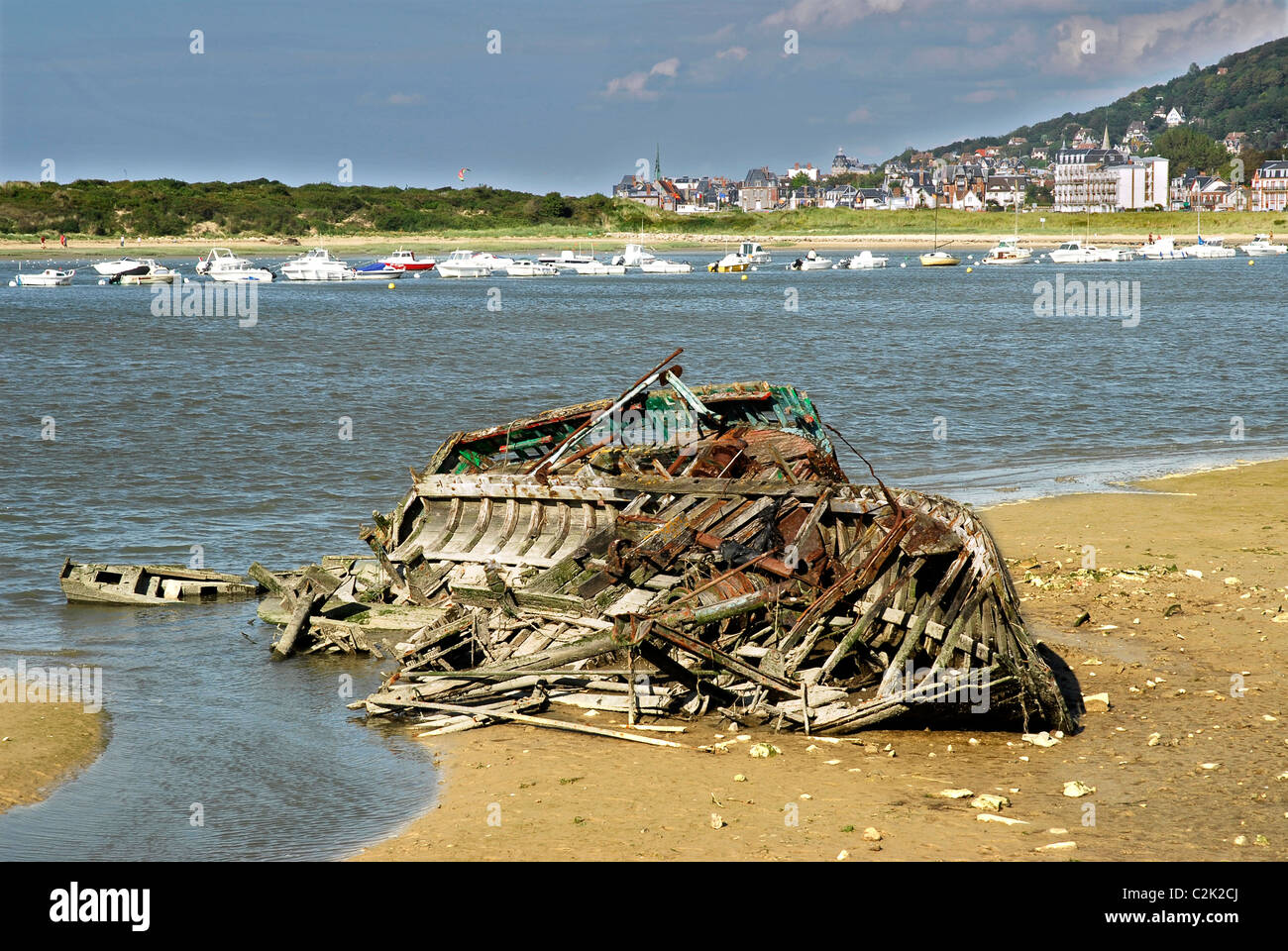 Shipwreck boat on the beach of Dives sur Mer in France with the commune of Hougalte in the background Stock Photo