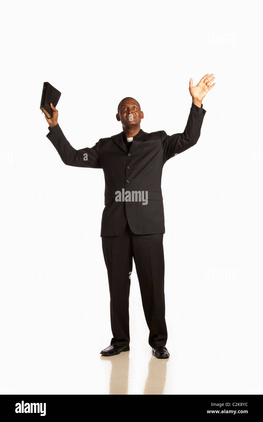 A Man Wearing A Clerical Collar And Holding His Bible Up With Hands Raised And Looking Up Stock Photo