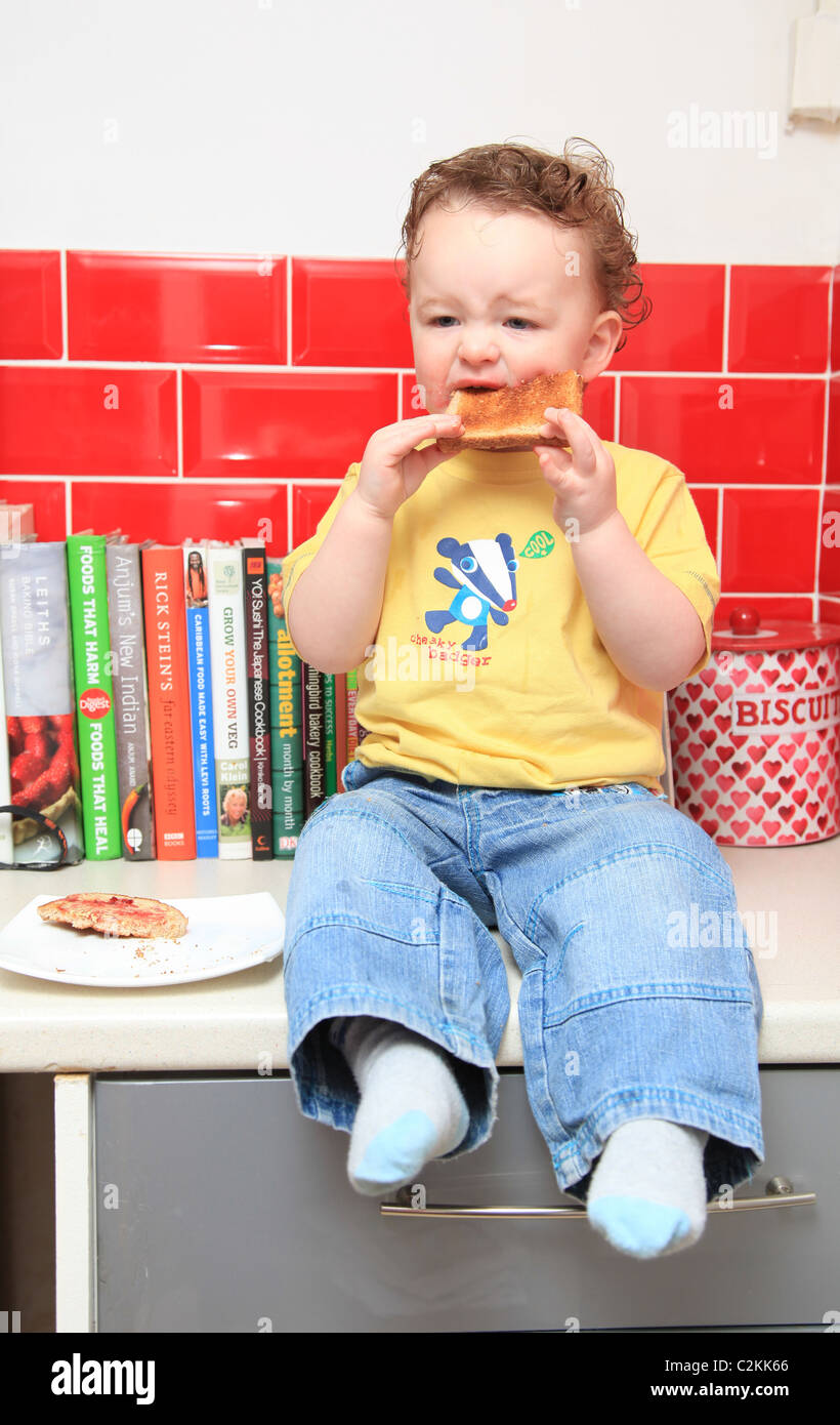 Toddler boy sitting on kitchen counter eating toast Stock Photo - Alamy