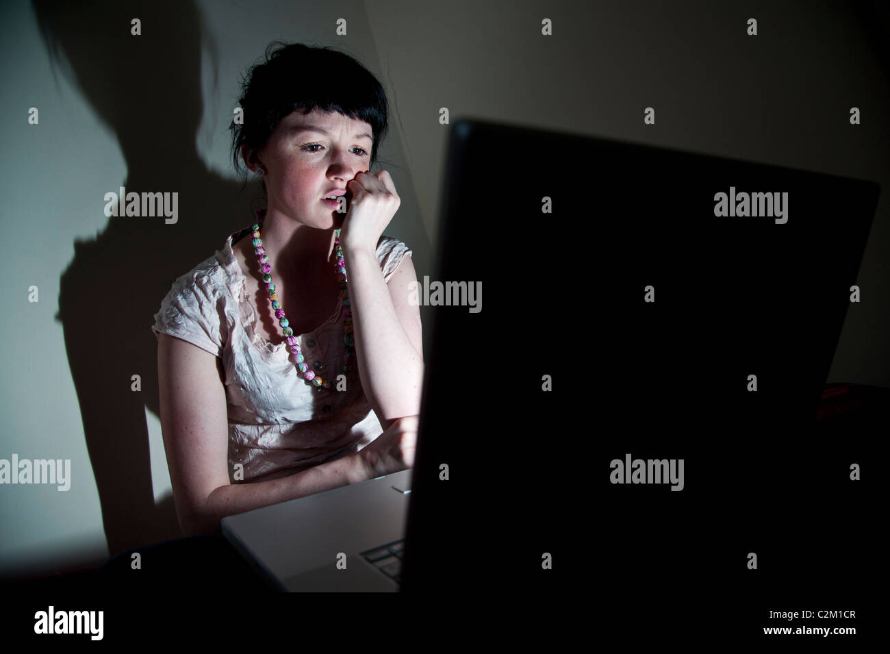 A young woman UK university student working on her laptop computer in bedroom at home, worried about email virus bug facebook Stock Photo