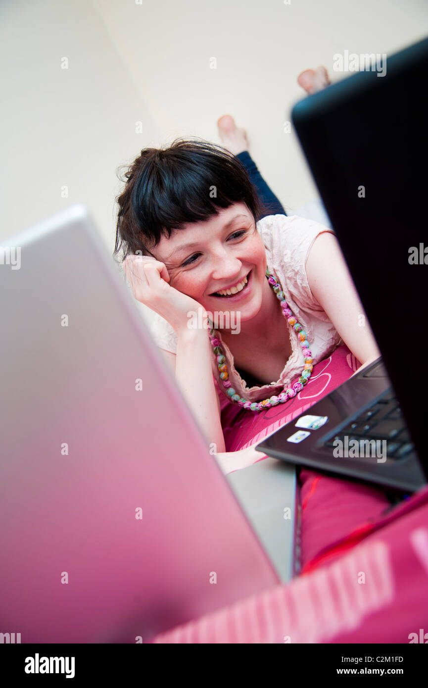 A happy smiling young woman UK university student working on two laptop computer in her bedroom at home Stock Photo