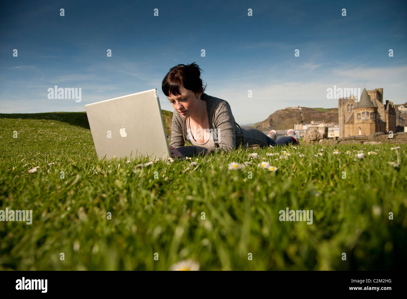 A young woman UK Aberystwyth university student working on her apple laptop computer outdoors on a sunny warm day Stock Photo