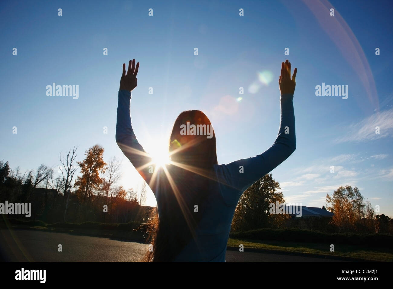 Beams Of Sunlight And A Circular Glare Around A Teenage Girl With Her Hands Raised Stock Photo
