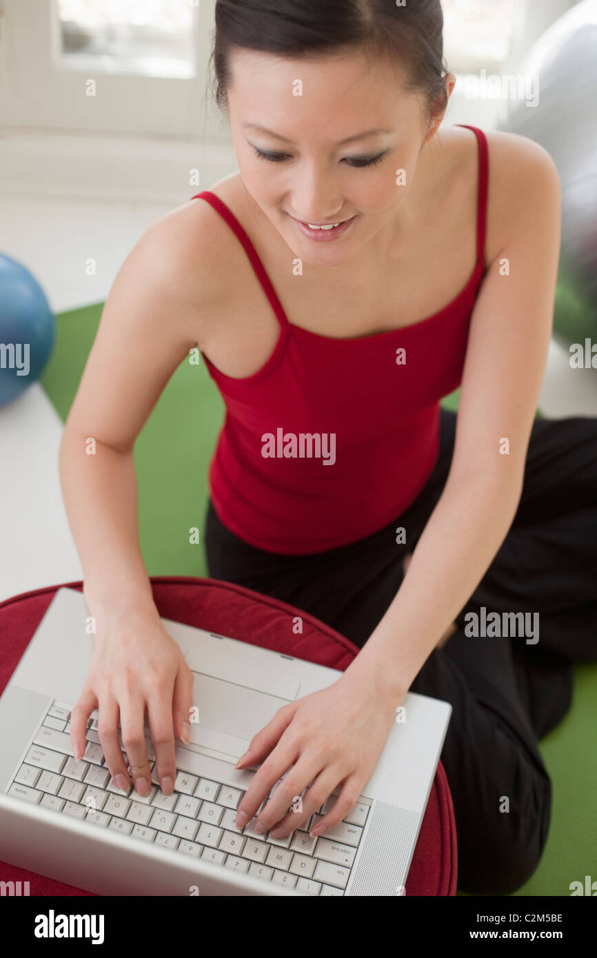 Beautiful Asian woman sitting on an exercise mat using her laptop Stock ...