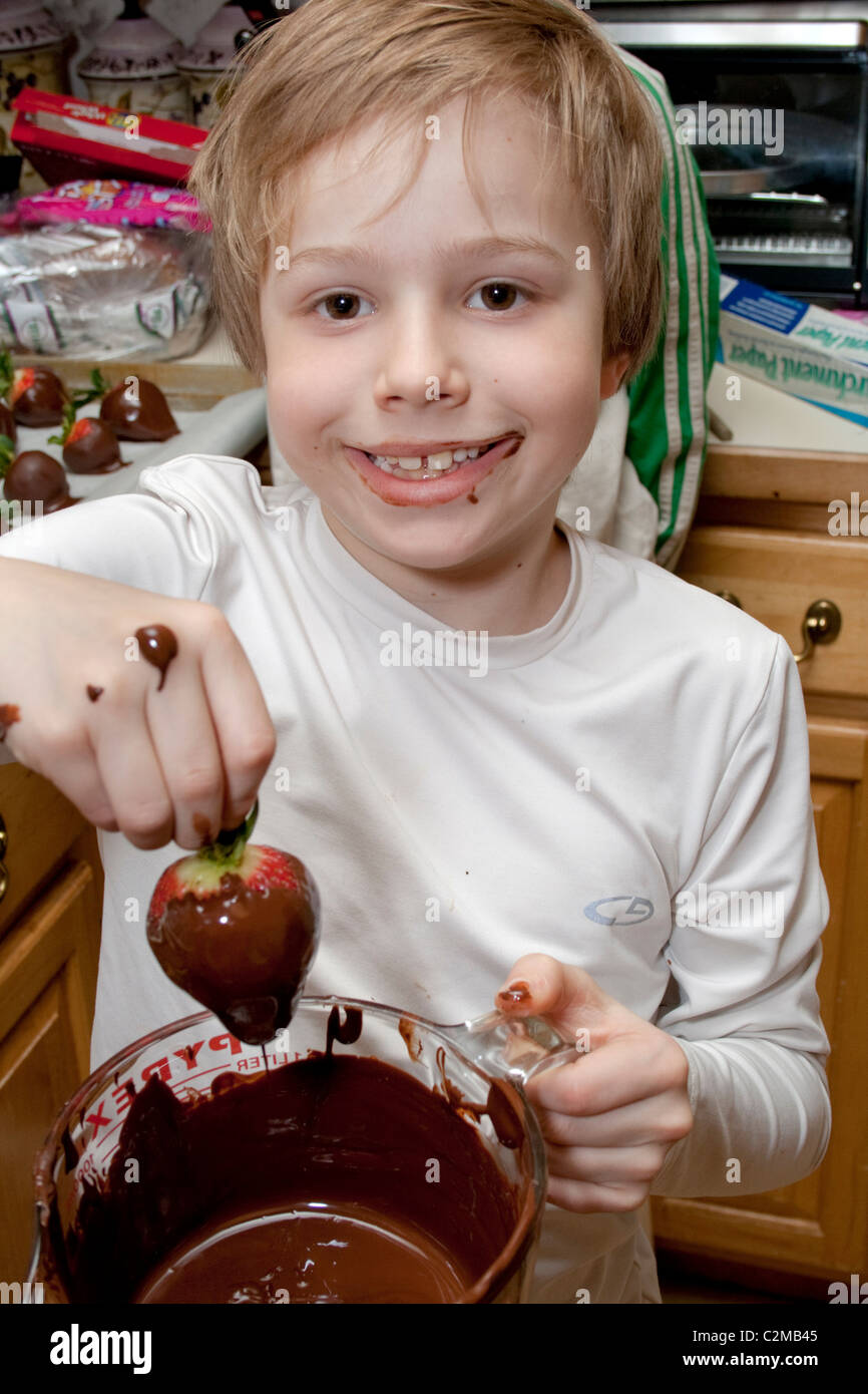 Happy boy age 8 dipping strawberry into chocolate. St Paul Minnesota MN USA Stock Photo