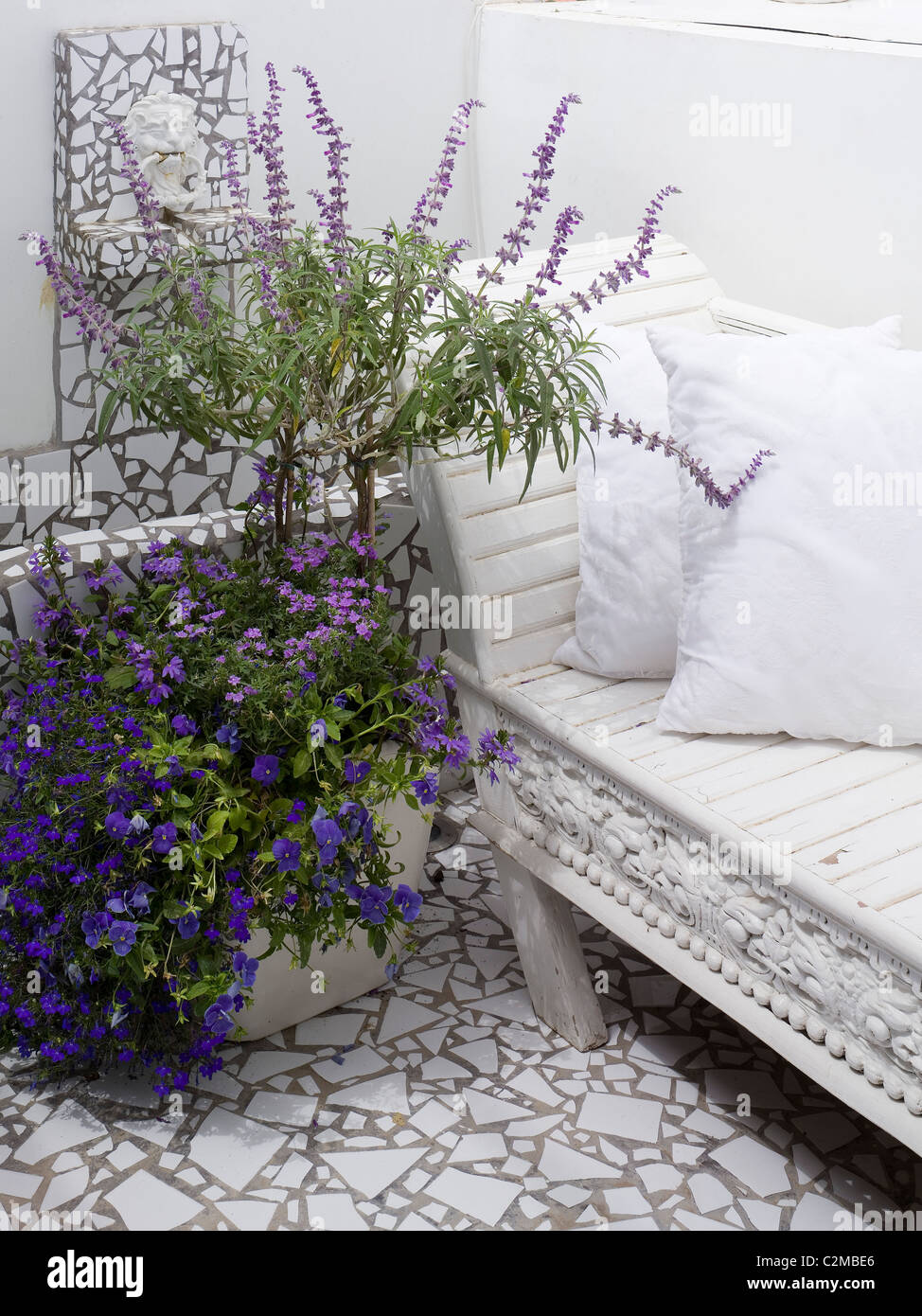 Detail of white terrazzo tiling, white wooden seating and blue and mauve flowers in pot Stock Photo