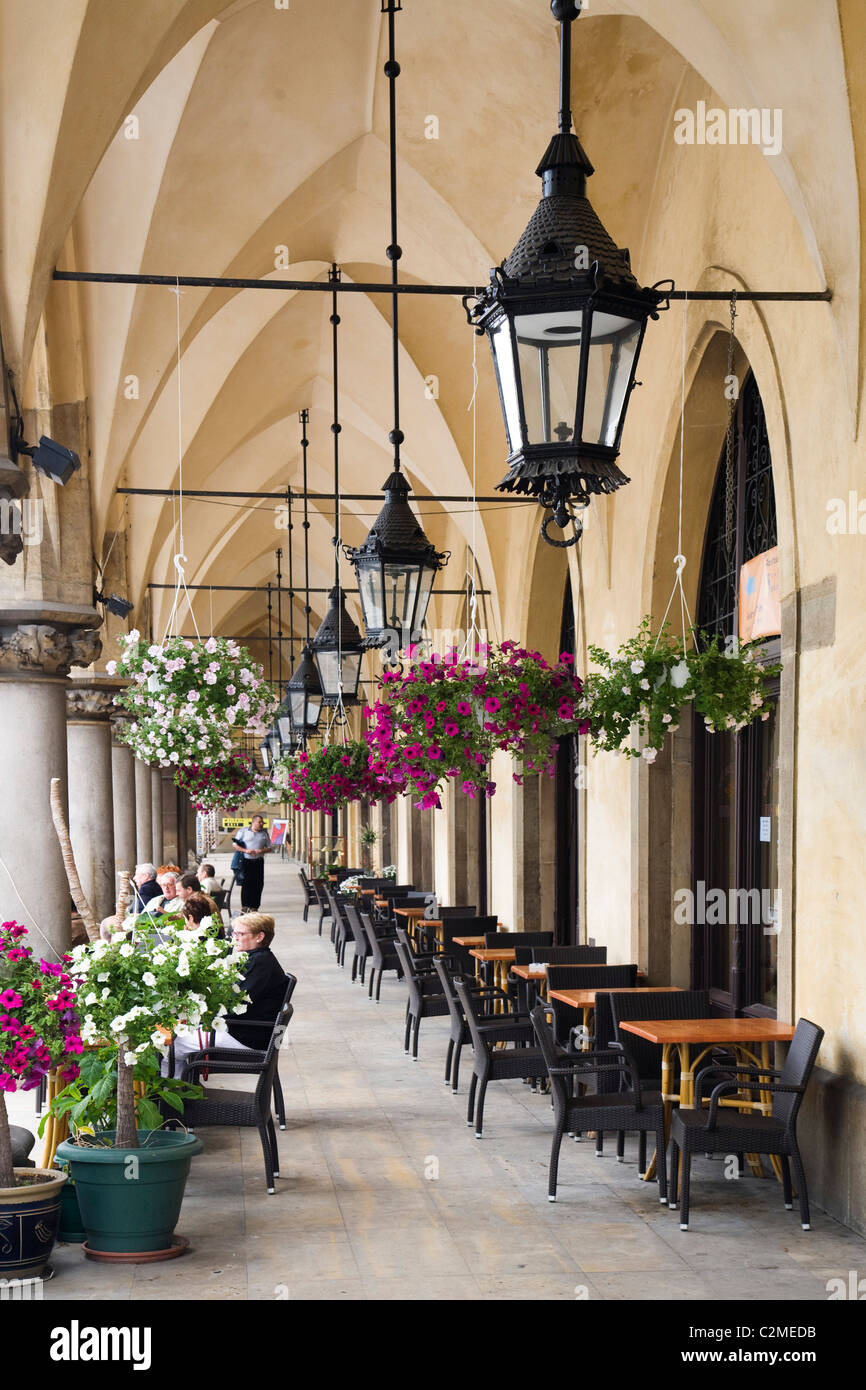 Colourful flowers and hanging baskets outside a cafe on a arched walkway outside the Cloth Hall or Sukiennice in the Rynek Stock Photo