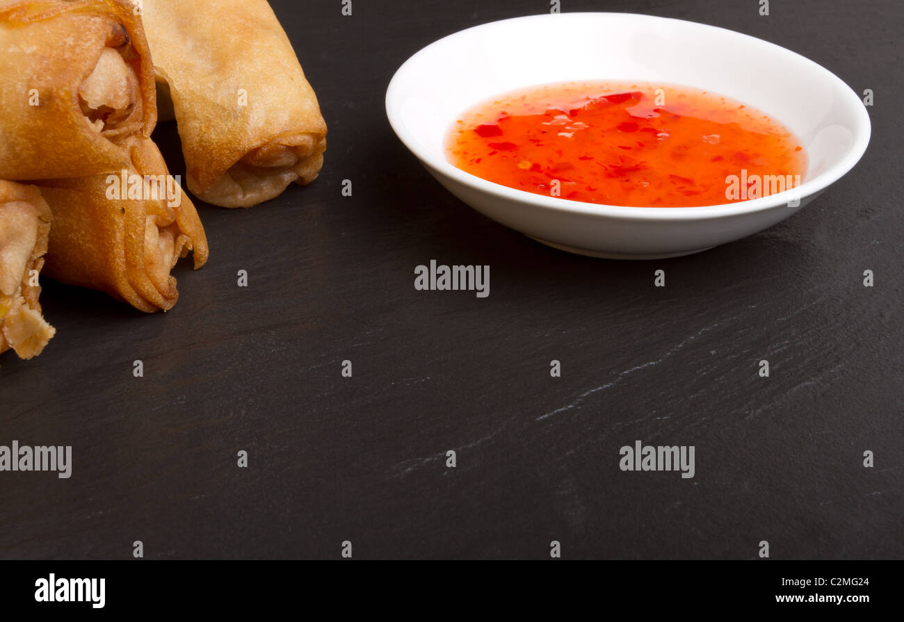 Spring rolls with sweet chili dipping sauce on dark grey slate background. Stock Photo